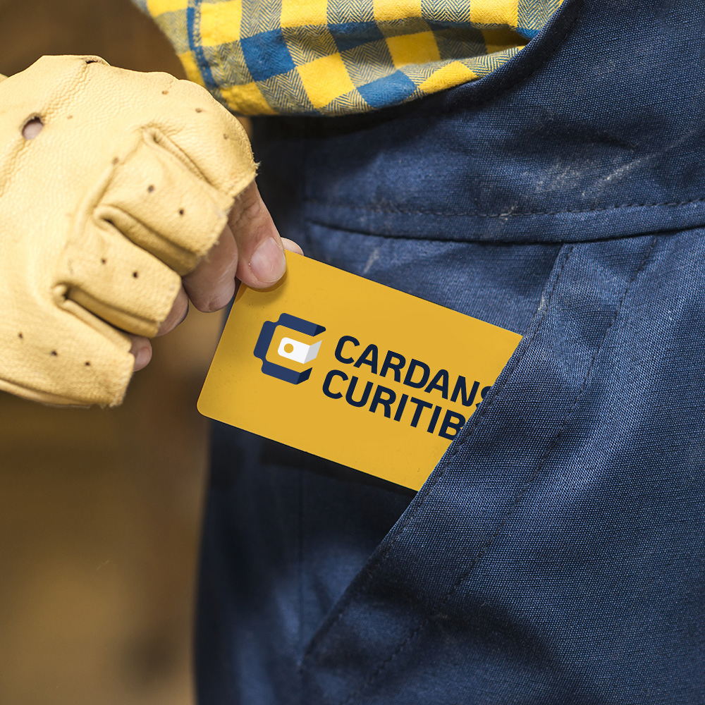 A close-up of a person showing a business card with the 'Cardans Curitiba' logo on a dark yellow background.